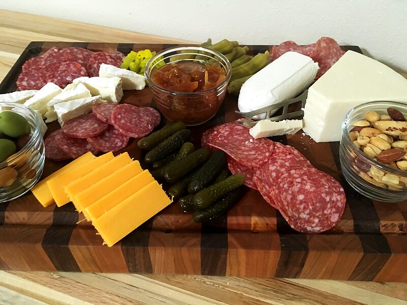 Charcuterie board loaded with cheese, salami, pickles and nuts