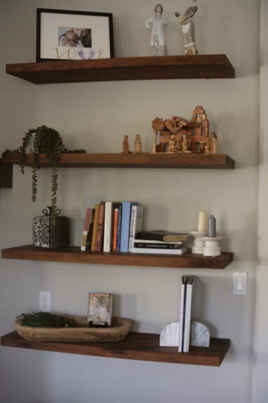 Three floating walnut shelves holding books, plants and framed photos