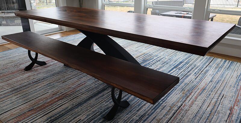 The walnut table with a walnut bench in front, on its curved black steel base