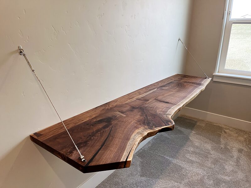 Floating live-edge walnut desk held at the wall and by two slim steel cables